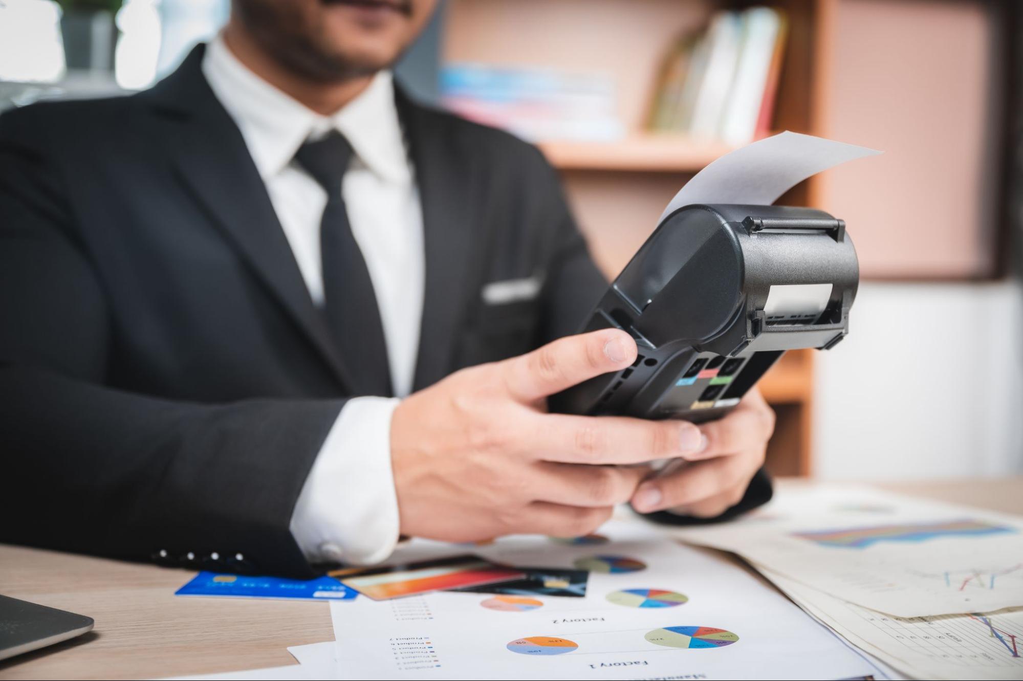 Person In A Suit Using A Handheld Payment Terminal With A Receipt Printing Out | Condor PH